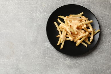 Photo of Delicious French fries with cheese sauce on grey table, top view. Space for text