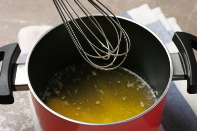 Photo of Pot with melting butter and whisk on table, closeup