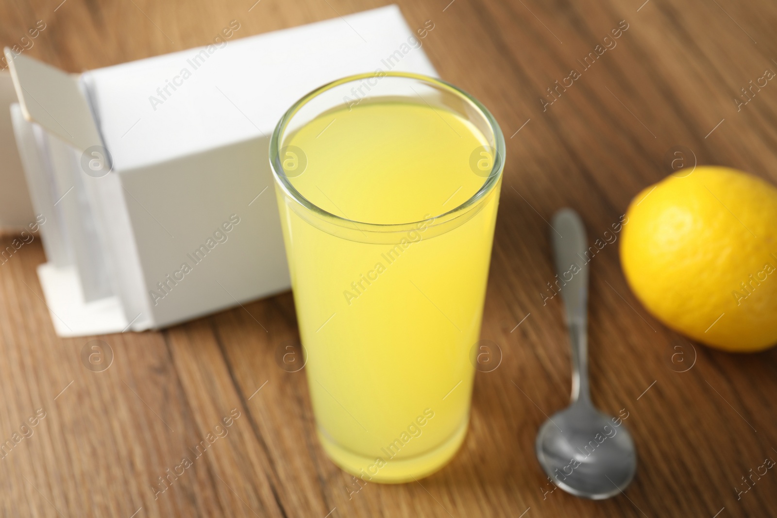 Photo of Glass with dissolved drug and box of medicine sachets on wooden table