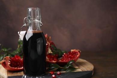 Photo of Tasty pomegranate sauce in bottle, fruits and branches on wooden table, closeup. Space for text