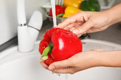 Photo of Woman washing paprika pepper in kitchen sink, closeup