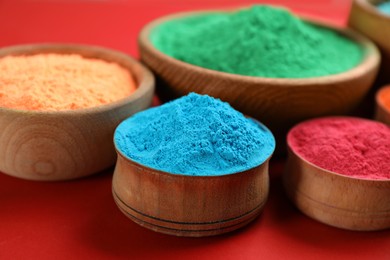 Photo of Colorful powders in wooden bowls on red background. Holi festival celebration