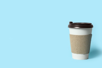 Takeaway paper coffee cup with cardboard sleeve on light blue background. Space for text