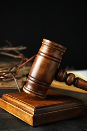 Photo of Wooden judge gavel and crown of thorns on black table, closeup