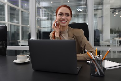 Photo of Happy woman working with laptop at black desk in office