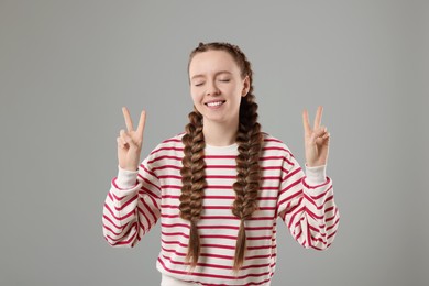 Photo of Woman with braided hair showing peace sign on grey background