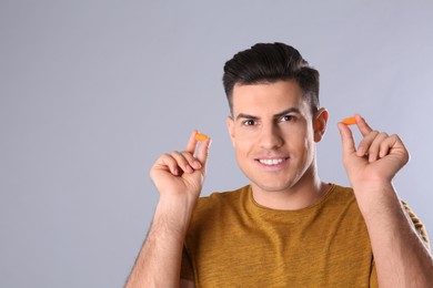 Man with foam ear plugs on grey background. Space for text