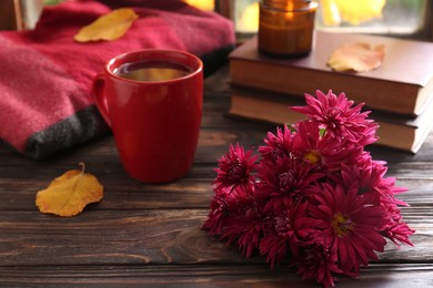 Photo of Beautiful chrysanthemum flowers and cup of hot drink on wooden table indoors. Autumn still life