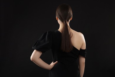 Woman in elegant dress on black background, back view