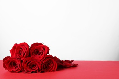 Photo of Beautiful roses on red table against white background. Space for text
