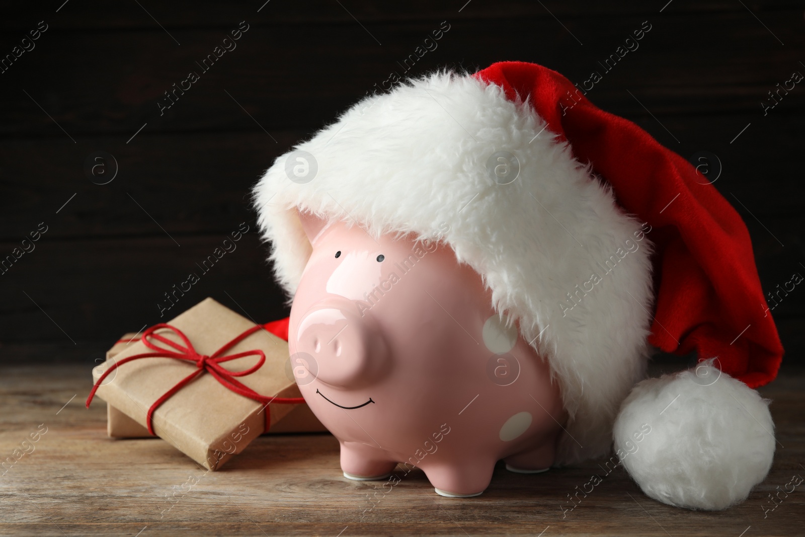 Photo of Piggy bank with Santa hat and gift boxes on wooden table against black background