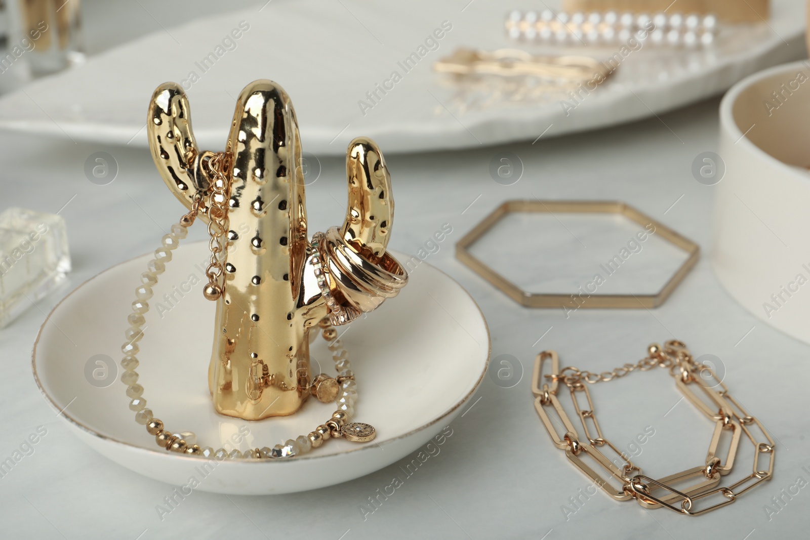 Photo of Decorative cactus with stylish golden bijouterie on white marble table, closeup