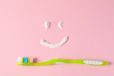 Photo of Funny face made with toothpaste and brush on pink background, flat lay