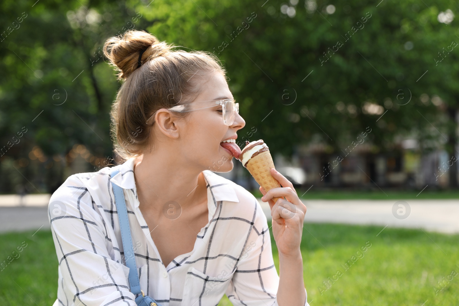 Photo of Young happy woman eating ice cream in park. Space for text