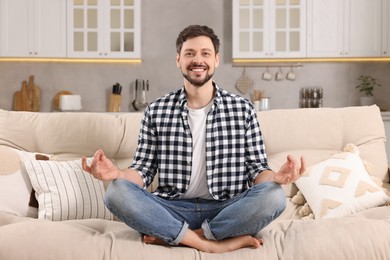 Photo of Happy man meditating on sofa at home. Harmony and zen