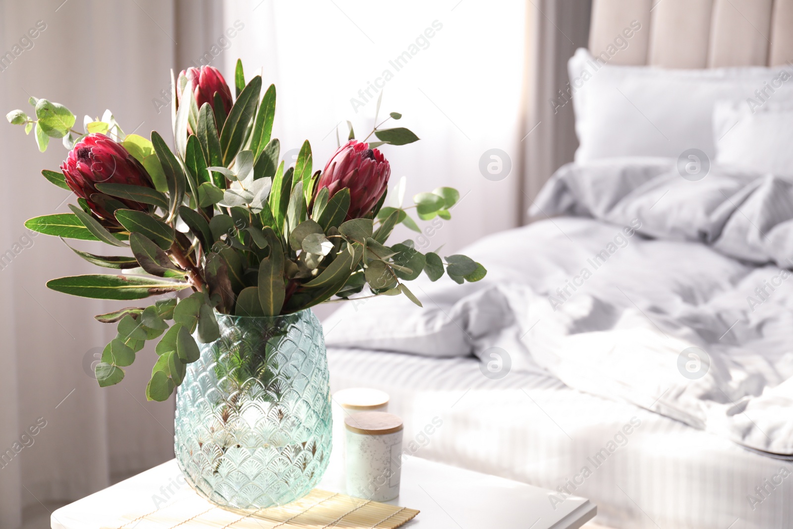 Photo of Vase with bouquet of beautiful Protea flowers on white table in bedroom