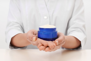 Female dermatologist holding jar of skin care product at table, closeup