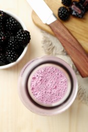 Photo of Delicious blackberry smoothie in glass bottle and fresh berries on wooden table, flat lay