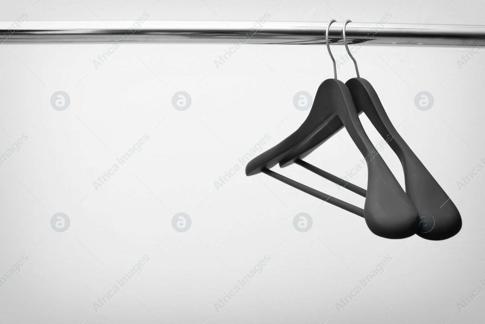 Photo of Clothes hangers on metal rail against light background