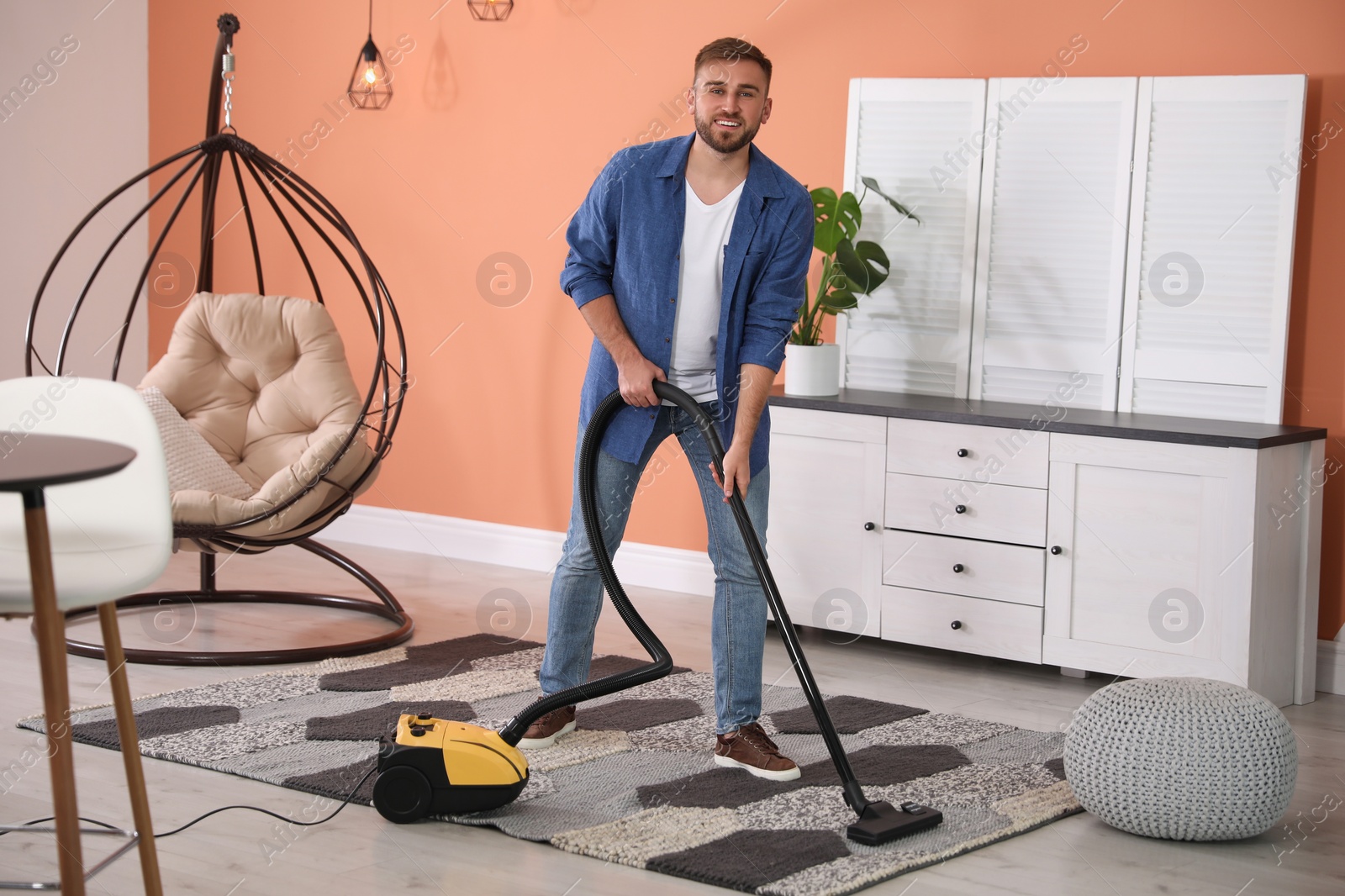 Photo of Young man using vacuum cleaner at home