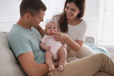 Photo of Happy couple holding their cute little baby with pacifier at home