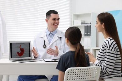 Gastroenterologist consulting woman with her daughter and showing image of stomach on laptop in clinic