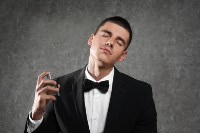 Photo of Handsome young man applying perfume on grey stone background