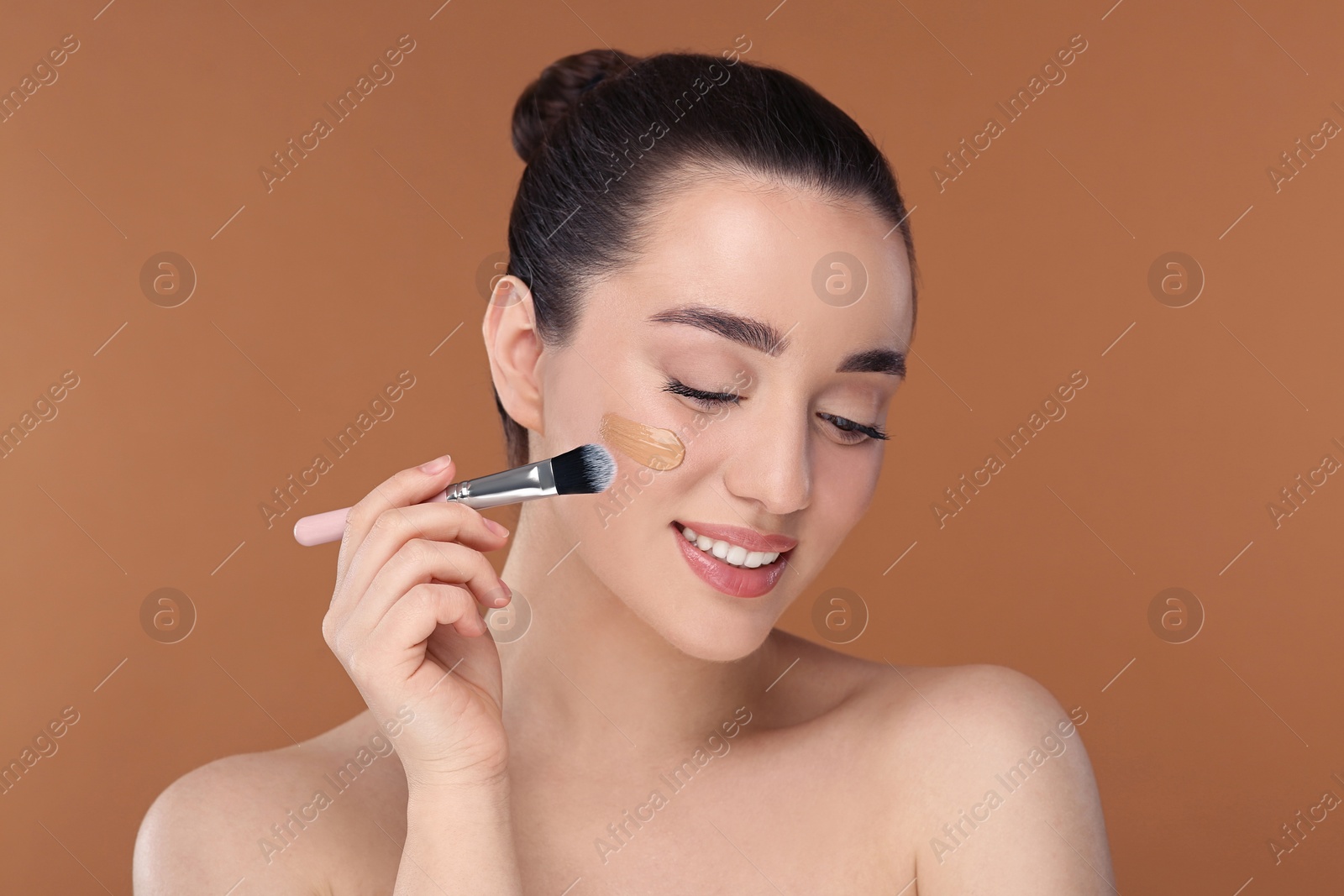 Photo of Woman applying foundation on face with brush against brown background