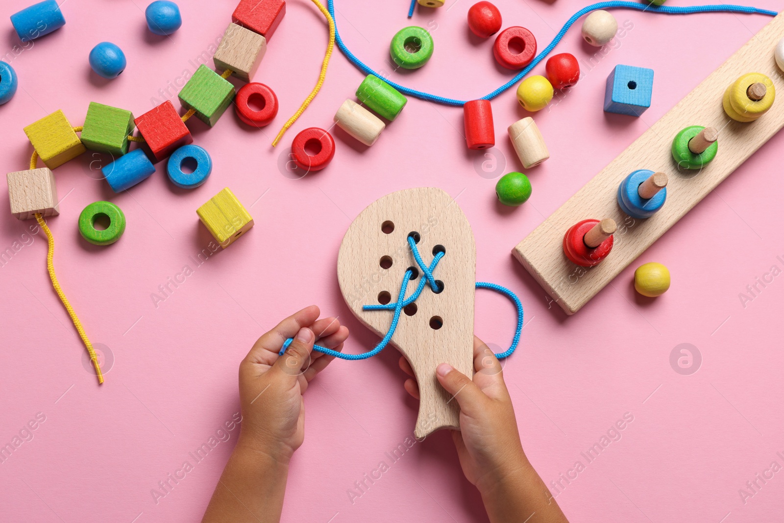 Photo of Motor skills development. Little child playing with wooden lacing toy at pink table, top view