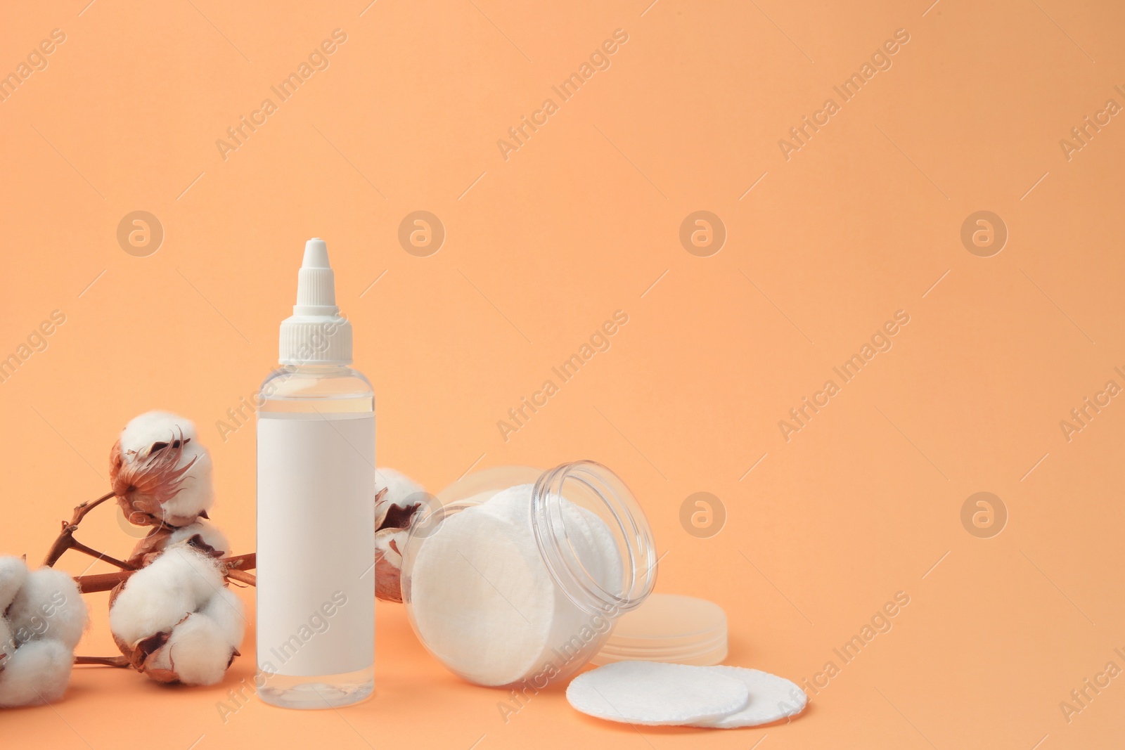 Photo of Composition with makeup remover and cotton flowers on pale orange background, space for text