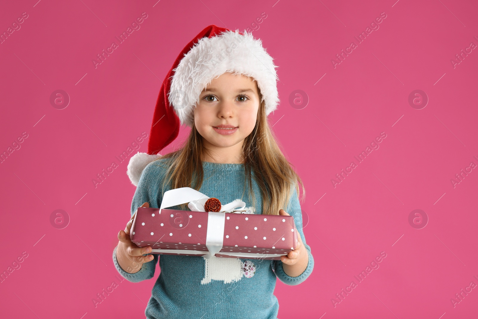 Photo of Cute child in Santa hat with Christmas gift on pink background