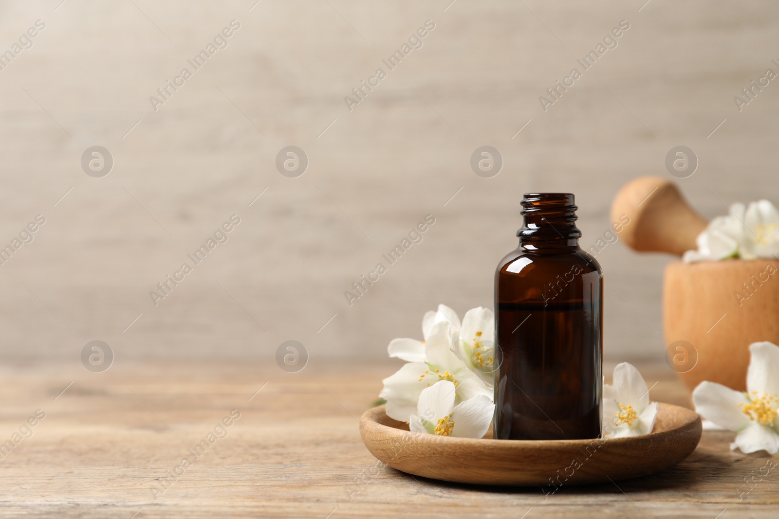 Photo of Jasmine essential oil and fresh flowers on wooden table, space for text