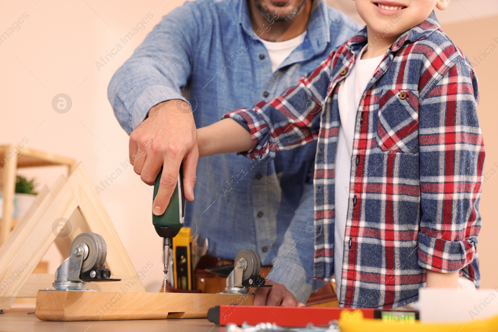 Photo of Father and son screwing wooden plank indoors, closeup. Repair work