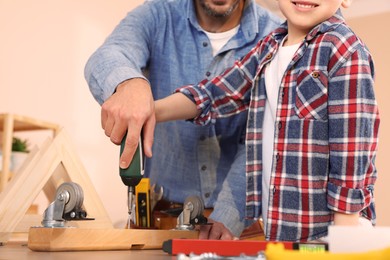 Photo of Father and son screwing wooden plank indoors, closeup. Repair work
