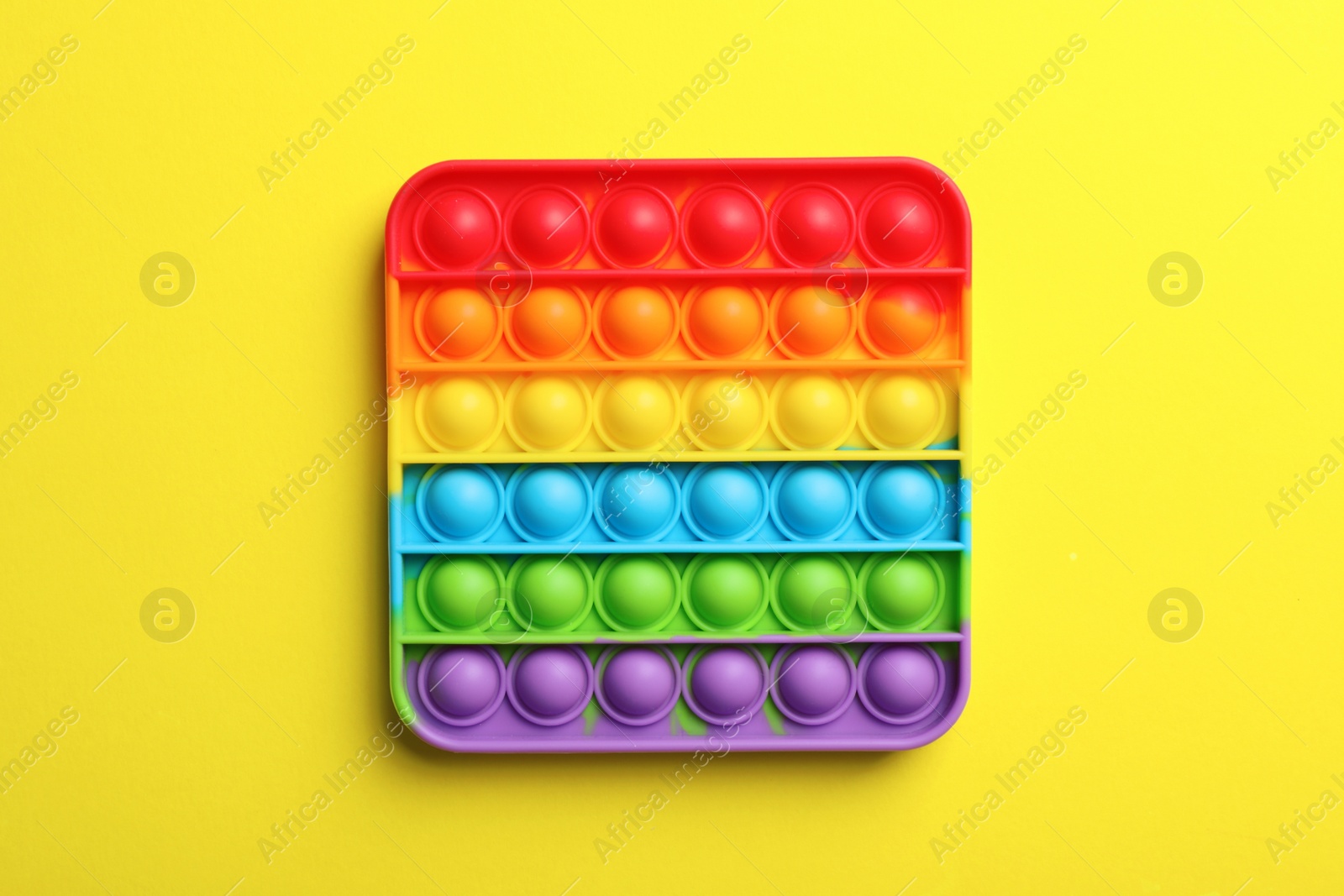 Photo of Rainbow pop it fidget toy on yellow background, top view
