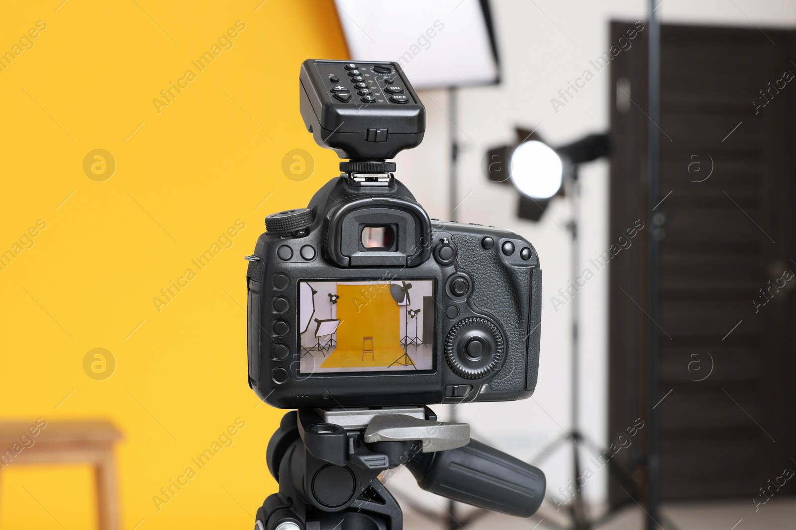 Photo of Tripod with camera, bar stool and professional lighting equipment in modern photo studio, focus on screen