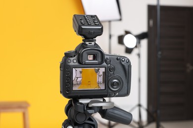 Tripod with camera, bar stool and professional lighting equipment in modern photo studio, focus on screen