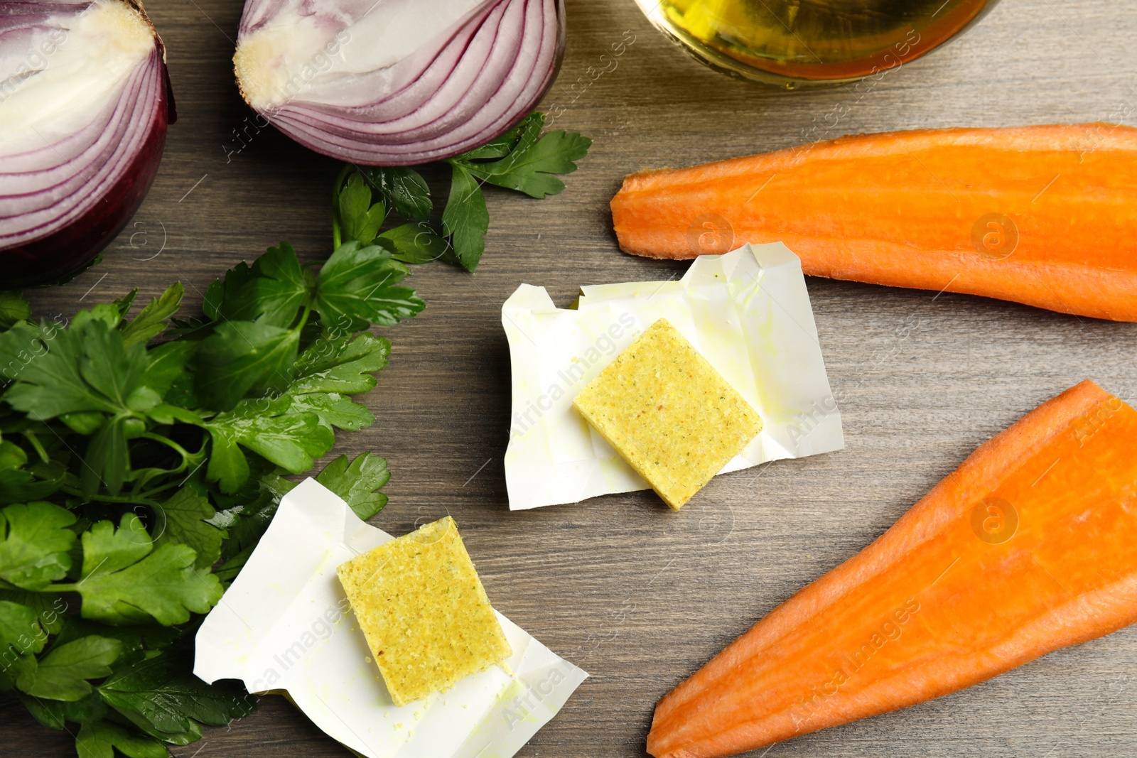 Photo of Bouillon cubes and other ingredients for soup on wooden table, flat lay