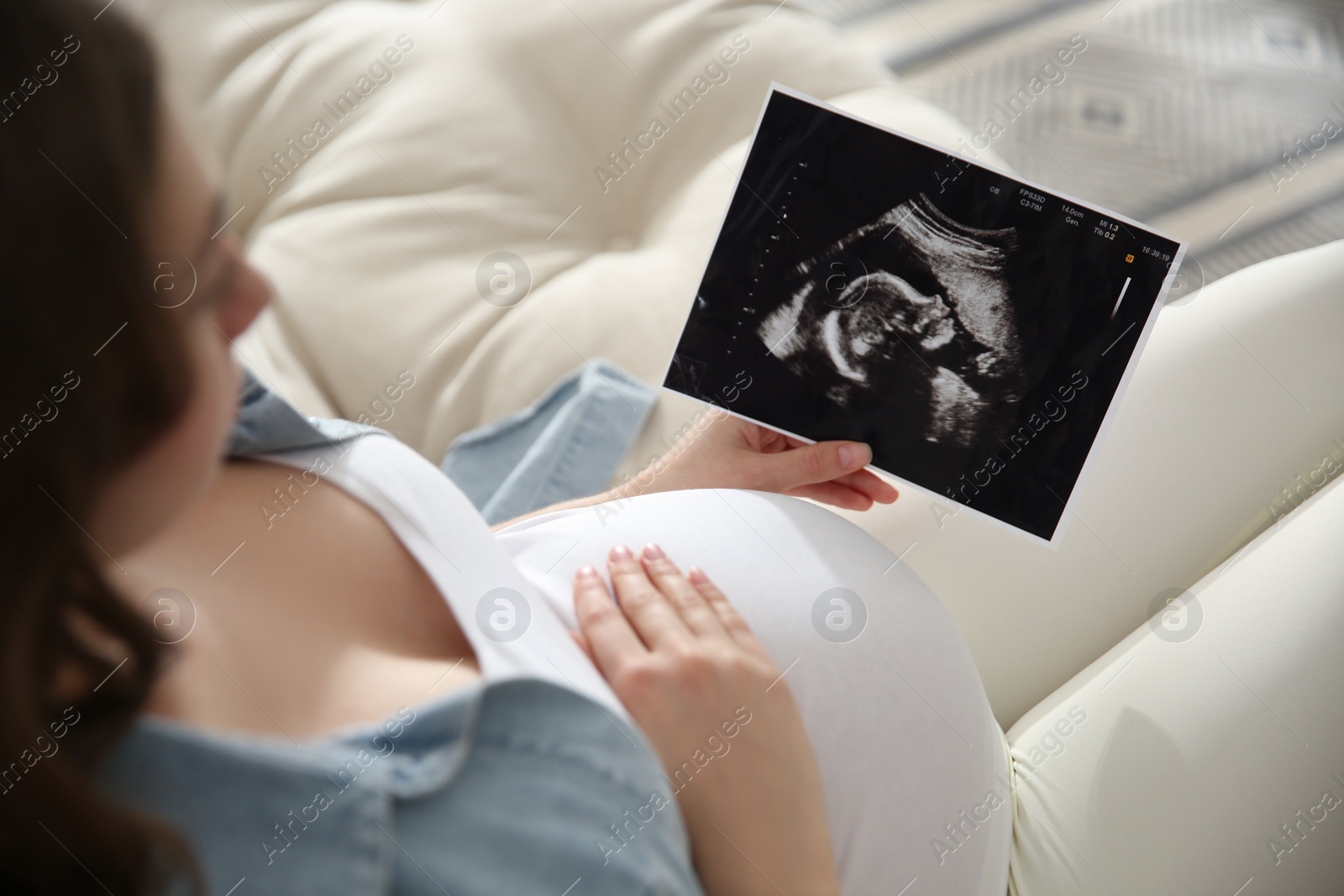 Photo of Pregnant woman holding ultrasound picture near her belly indoors, closeup