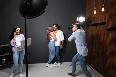 Photo of Professional photographer with assistant taking picture of young couple in modern studio