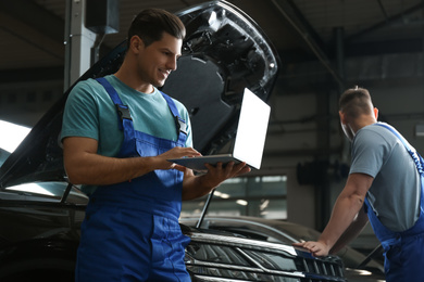 Photo of Mechanic with laptop doing car diagnostic at automobile repair shop