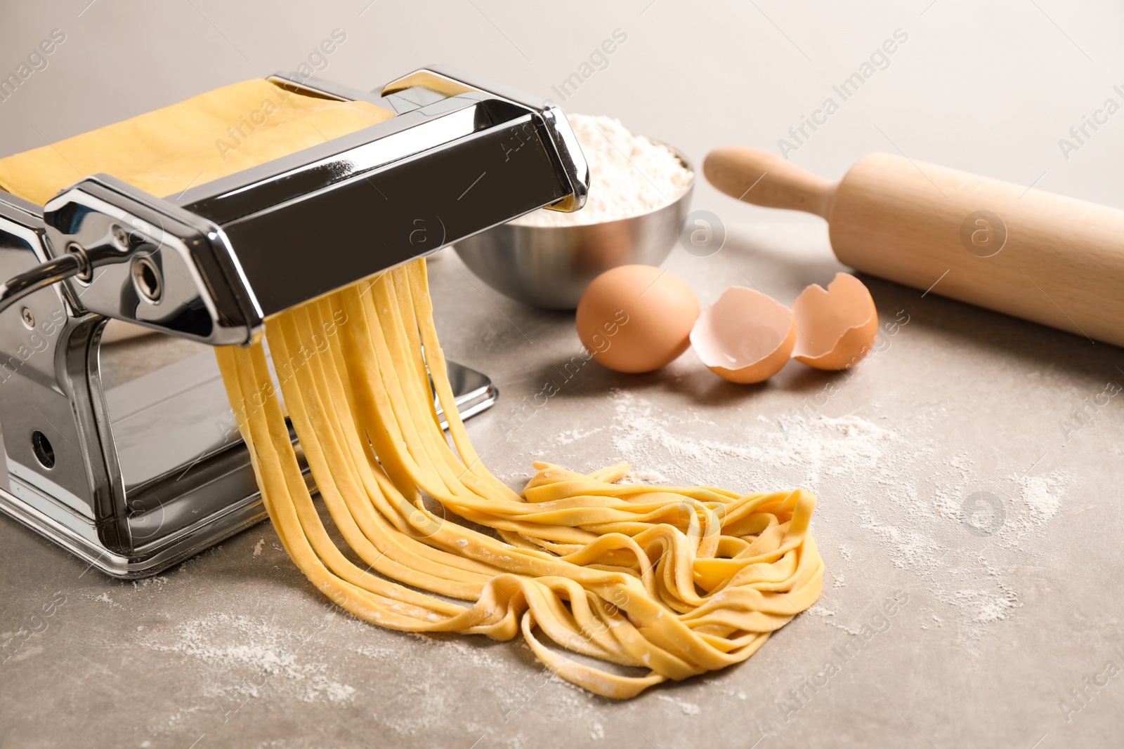 Photo of Pasta maker machine with dough and products on grey table