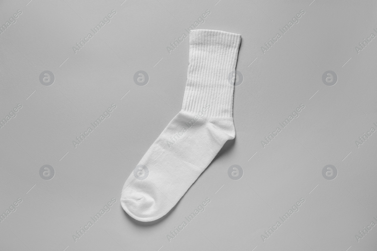 Photo of One white sock on light grey background, top view