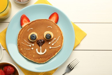 Creative serving for kids. Plate with cute cat made of pancakes, berries, cream, banana and chocolate paste on white wooden table, flat lay. Space for text