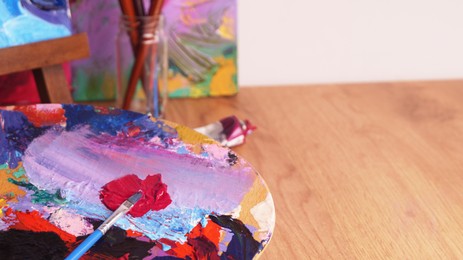 Photo of Artist's palette with mixed bright paints and brush indoors. Space for text