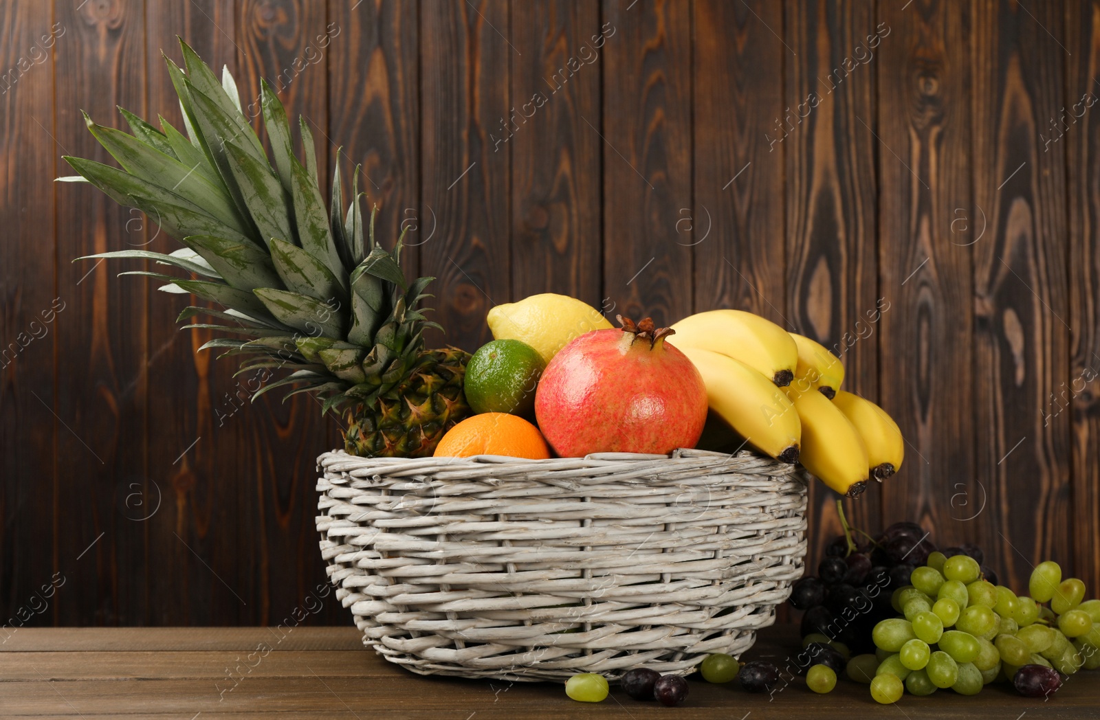 Photo of Wicker bowl with different ripe fruits on wooden table