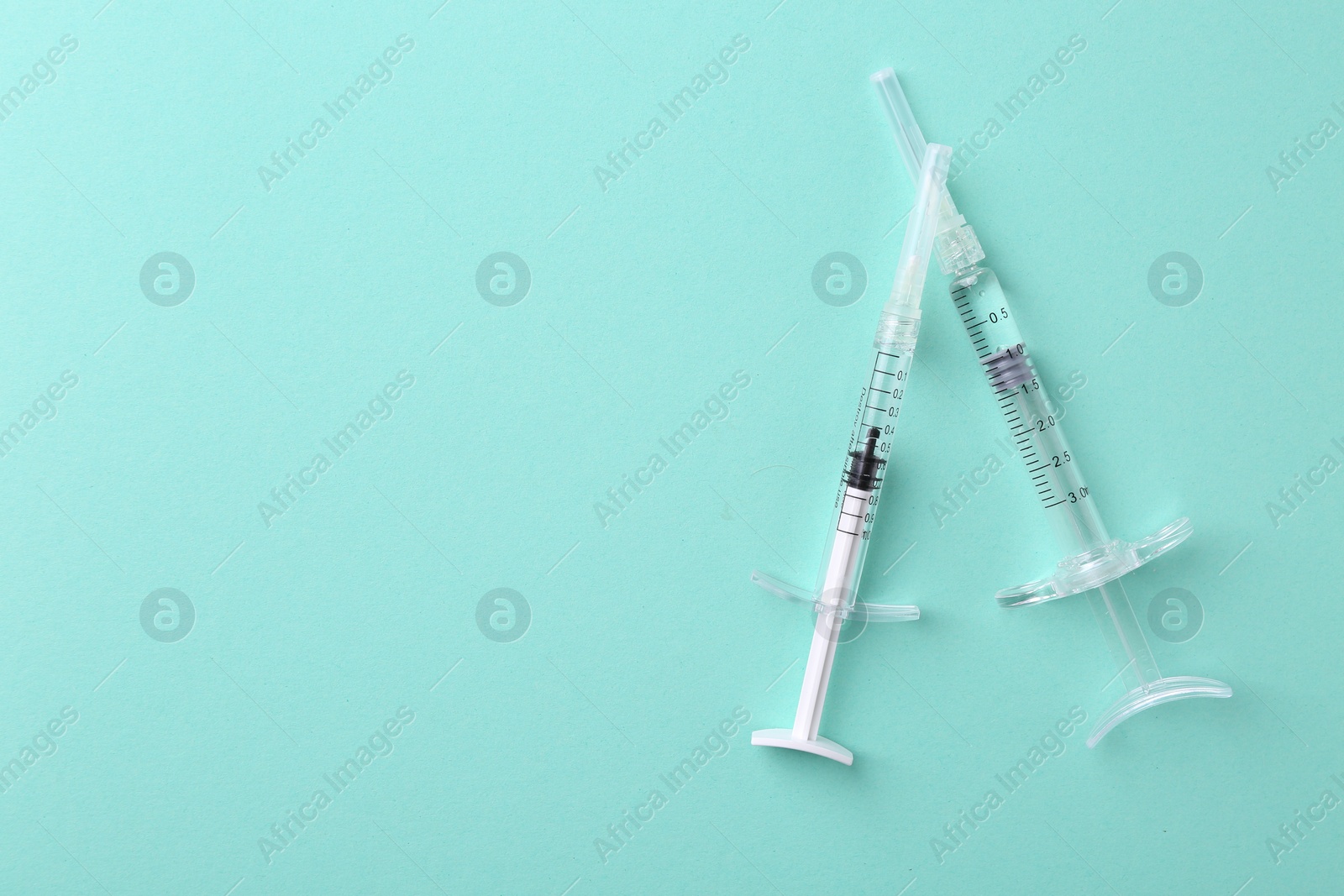 Photo of Injection cosmetology. Two medical syringes on turquoise background, top view. Space for text