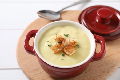 Tasty potato soup with croutons and rosemary in ceramic pot on white table, closeup