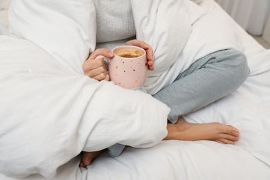 Woman with cup of coffee and soft blanket on bed, closeup