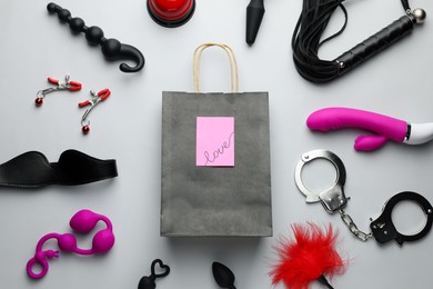 Photo of Flat lay composition with different sex toys and paper shopping bag on white background